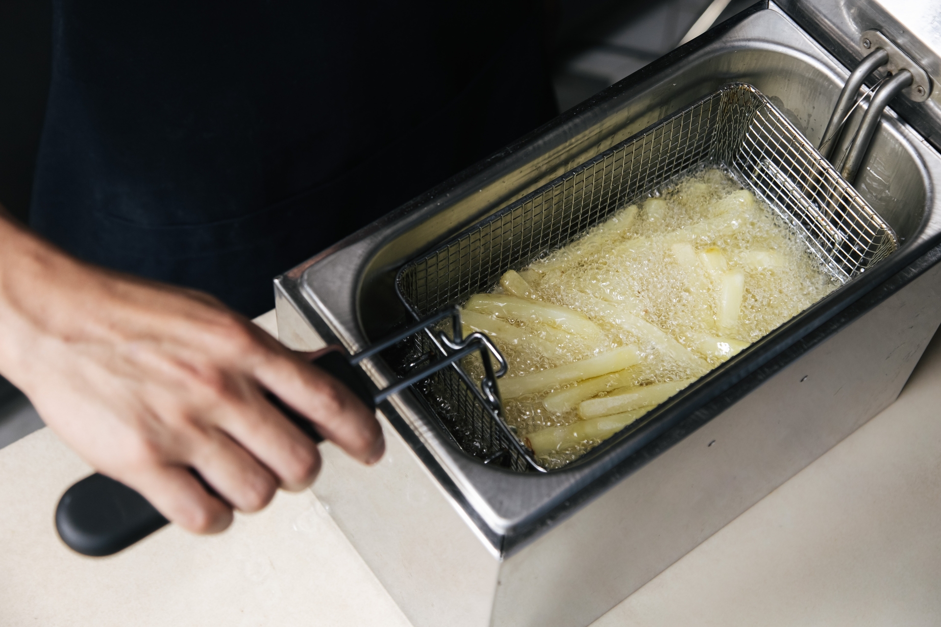 Pommes werden in Hand-Fritteuse in Frittierfett frittiert