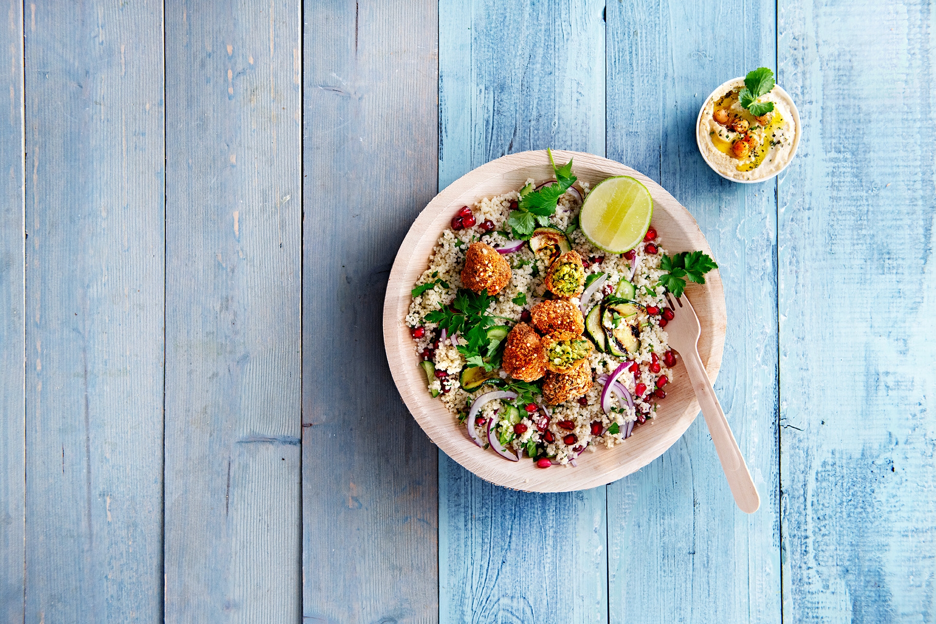 Falafel bites in Schale auf Couscous auf hellblauem Holztisch