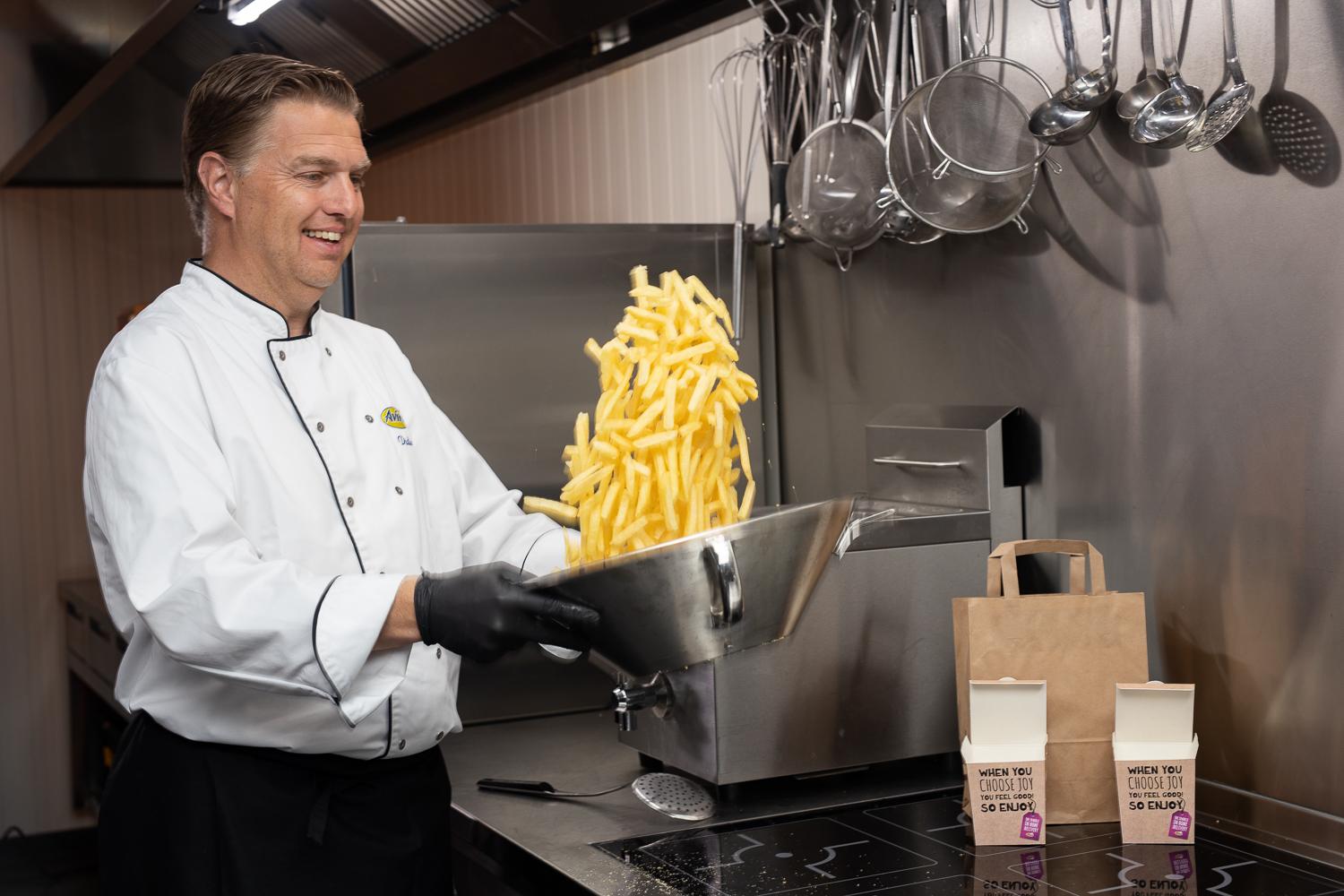 Küchen-Chef wirft Pommes in silberner Schale hoch um sie zu mixen