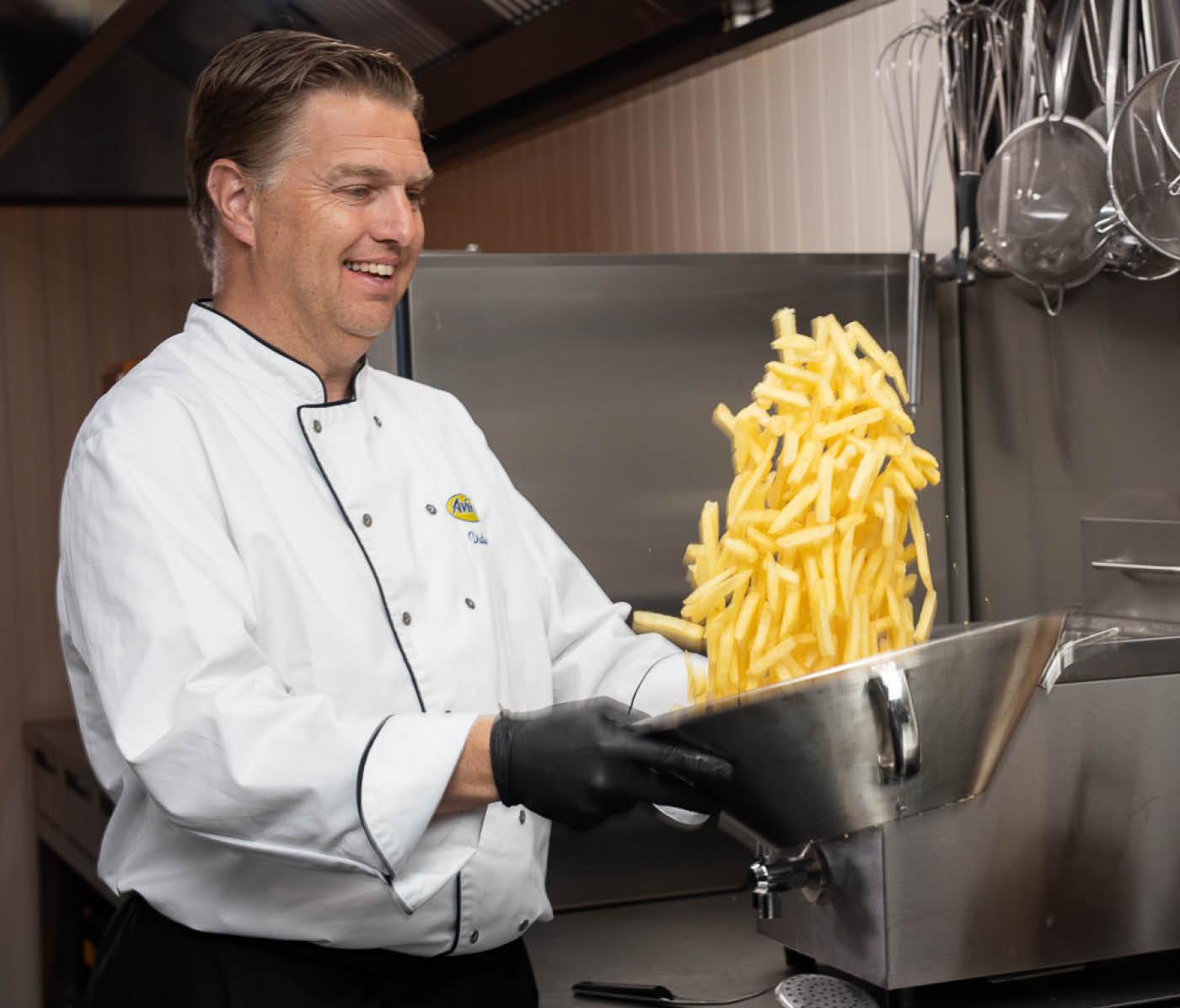 Küchen-Chef wirft Pommes in silberner Schale hoch um sie zu mixen
