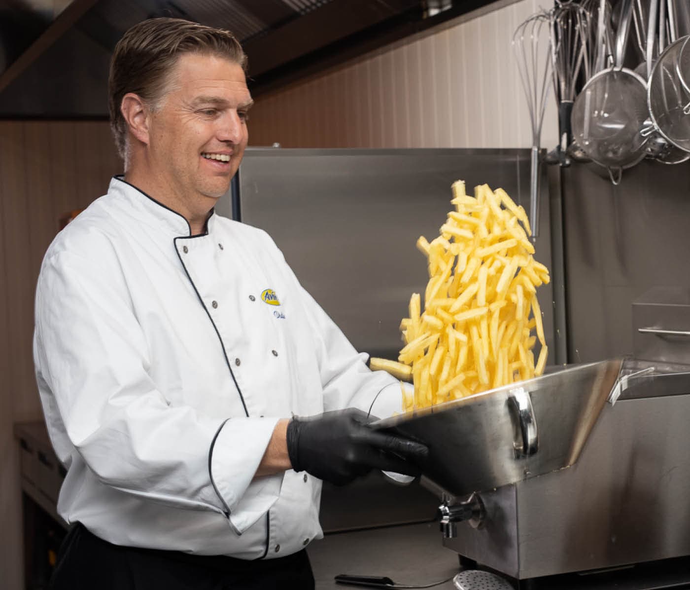 Küchen-Chef wirft Pommes in silberner Schale hoch um sie zu mixen
