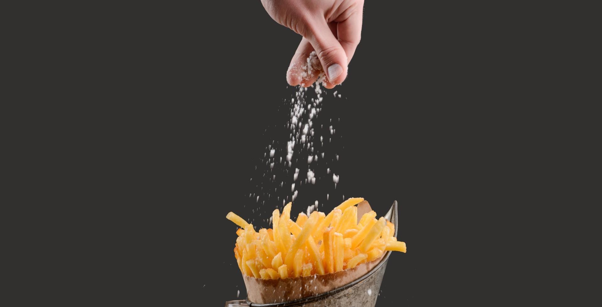 Pommes werden mit Salz vor dem servieren von Hand gewürzt