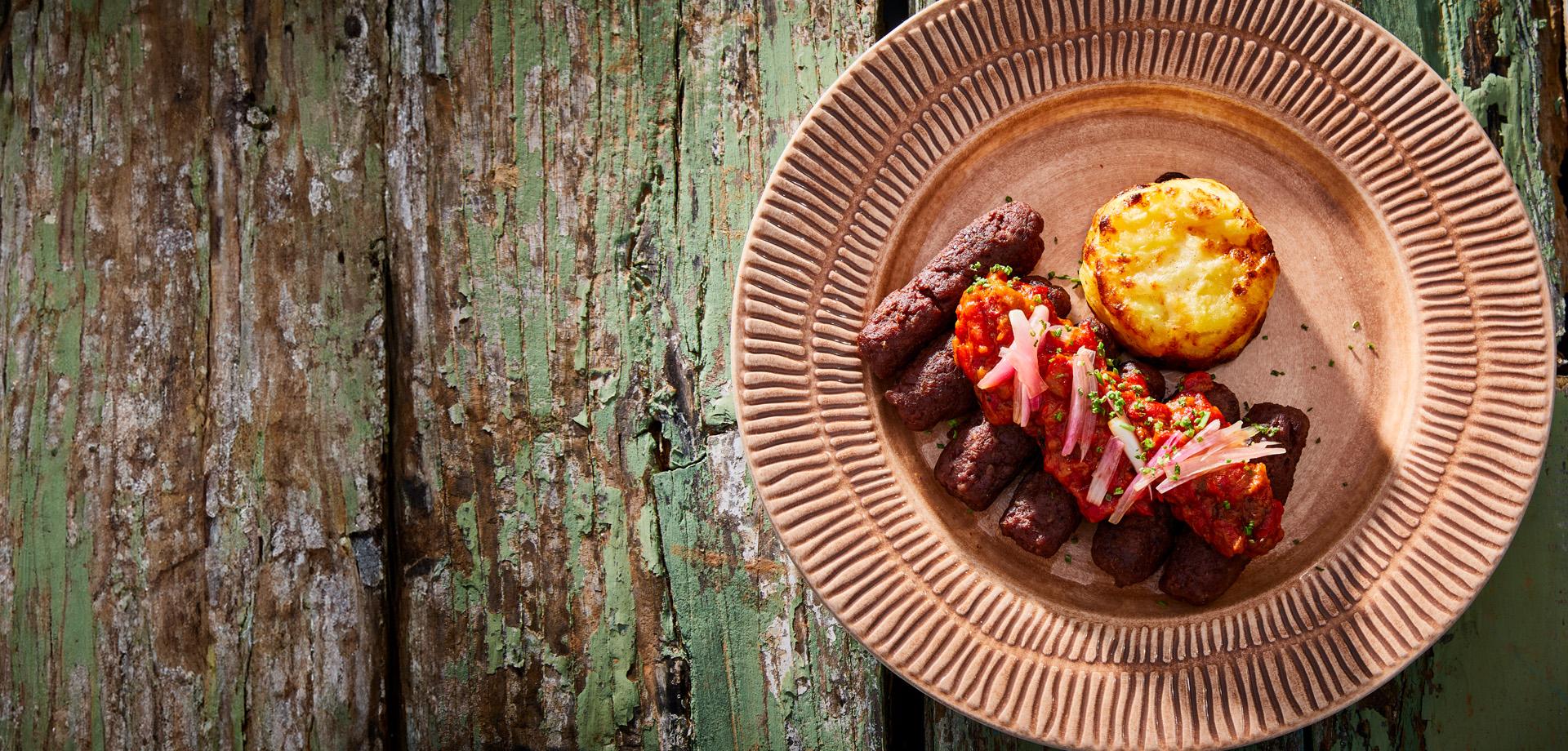 cevapcici auf grünem holztisch und rosa teller serviert mit aviko gratin