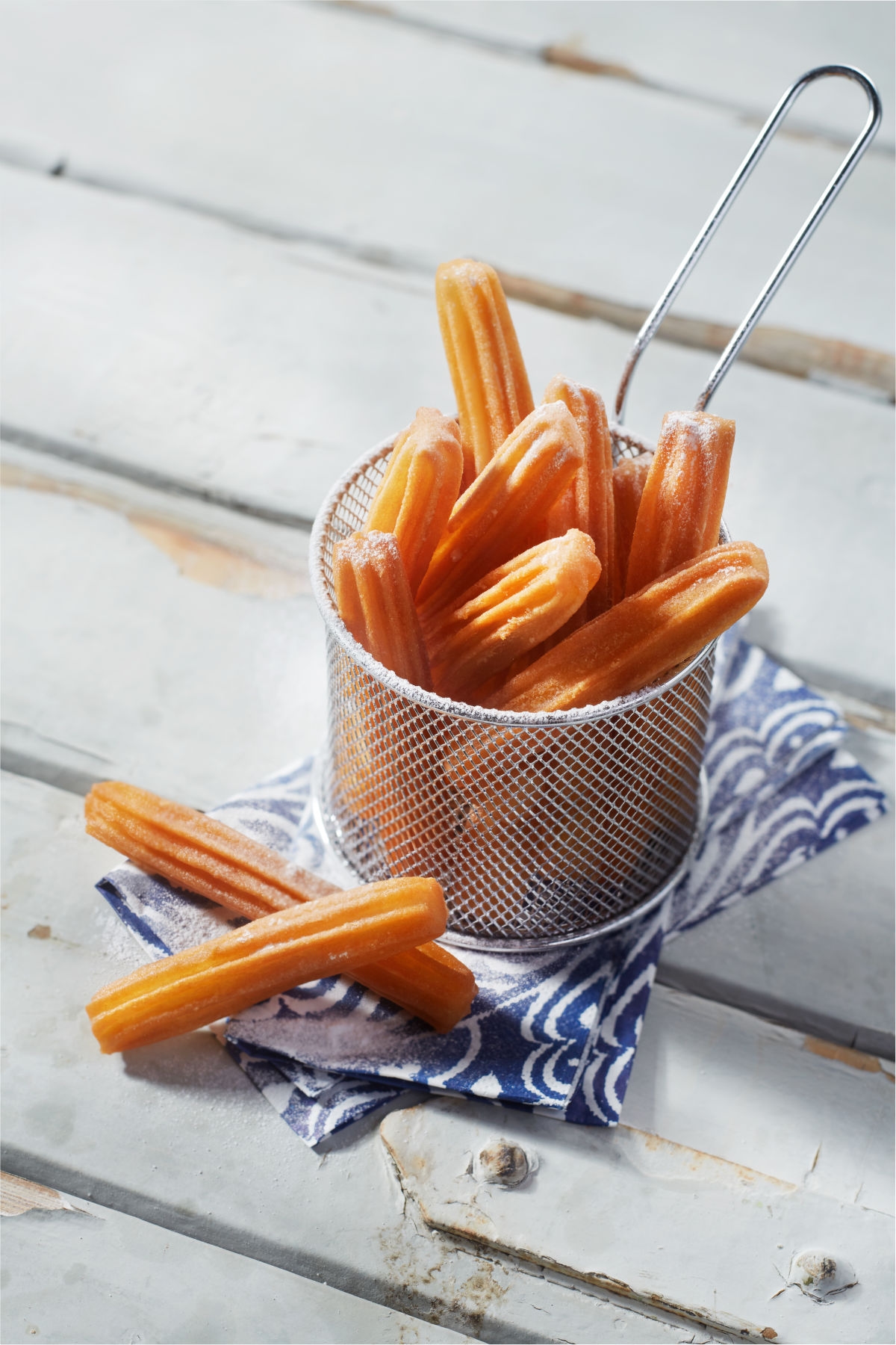 nachtisch in form von aviko churros serviert in einem metallkörbchen auf weissem holz