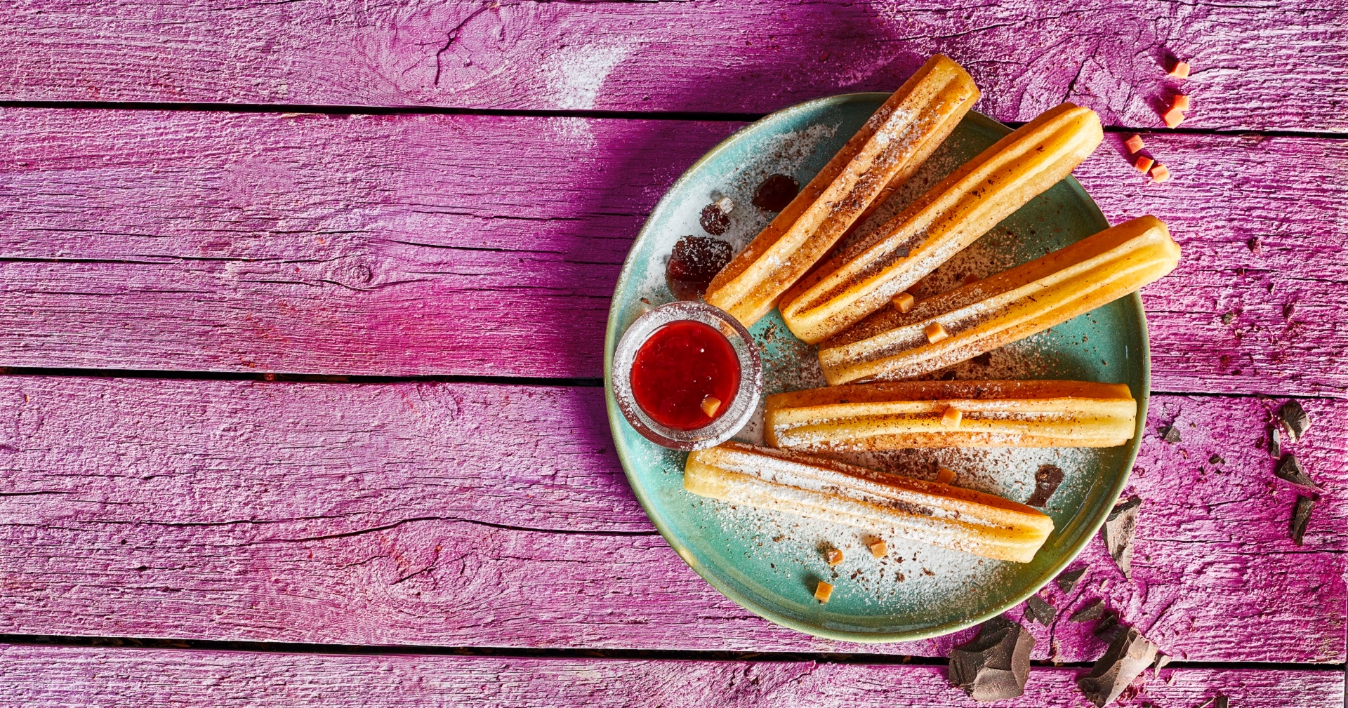 Header Foto Churros XXL super Gross Churros auf Teller auf pinkem Holztisch